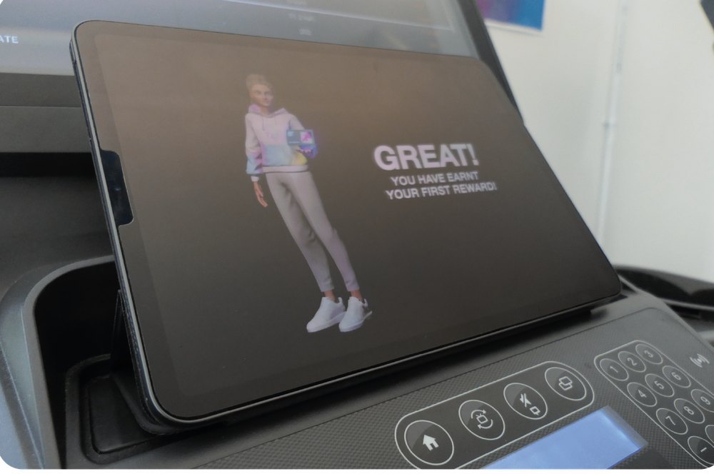A tablet on a treadmill showing an avatar and the message 'Great! You have earned your first reward'